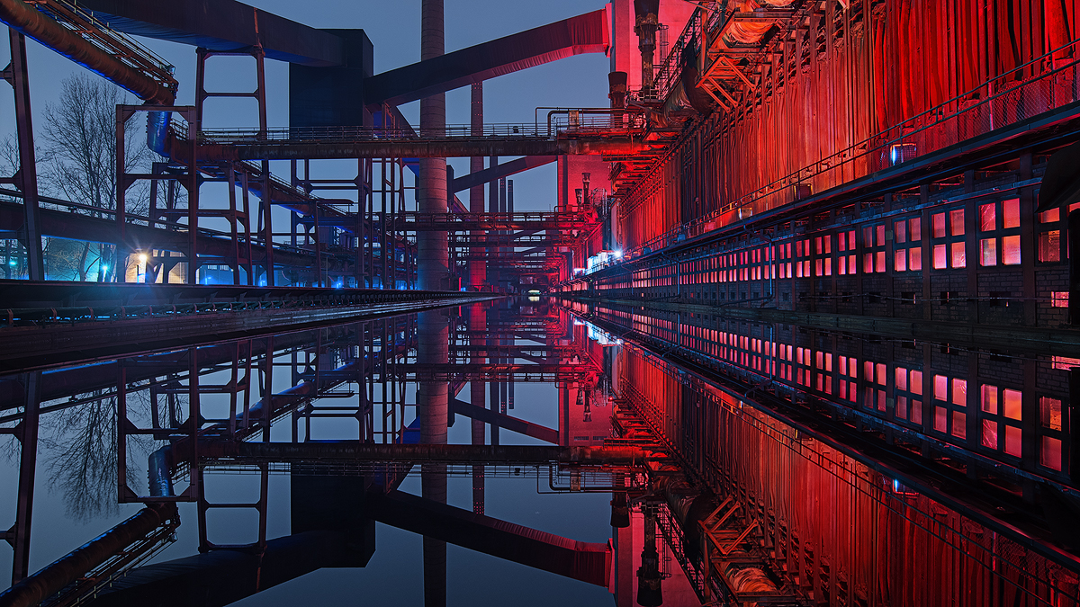 On a cold winter night the light installations on the former coking facility, now Unesco World Heritage, "Zeche Zollverein" located in Assindia tint the scenery in blue and red with a soft transition in between. The former pusher machine tracks are flooded with water and make for a terrific reflection in calm nights like this one.