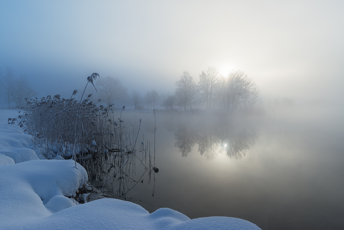 The sun shines through a veil of fog on a wintry morning in Bavaria. With the temperatures falling rapidly over night and the large body of water of the Kochelsee storing warmth from the day prior, the resulting steaming surface adds to the mysterious atmosphere.